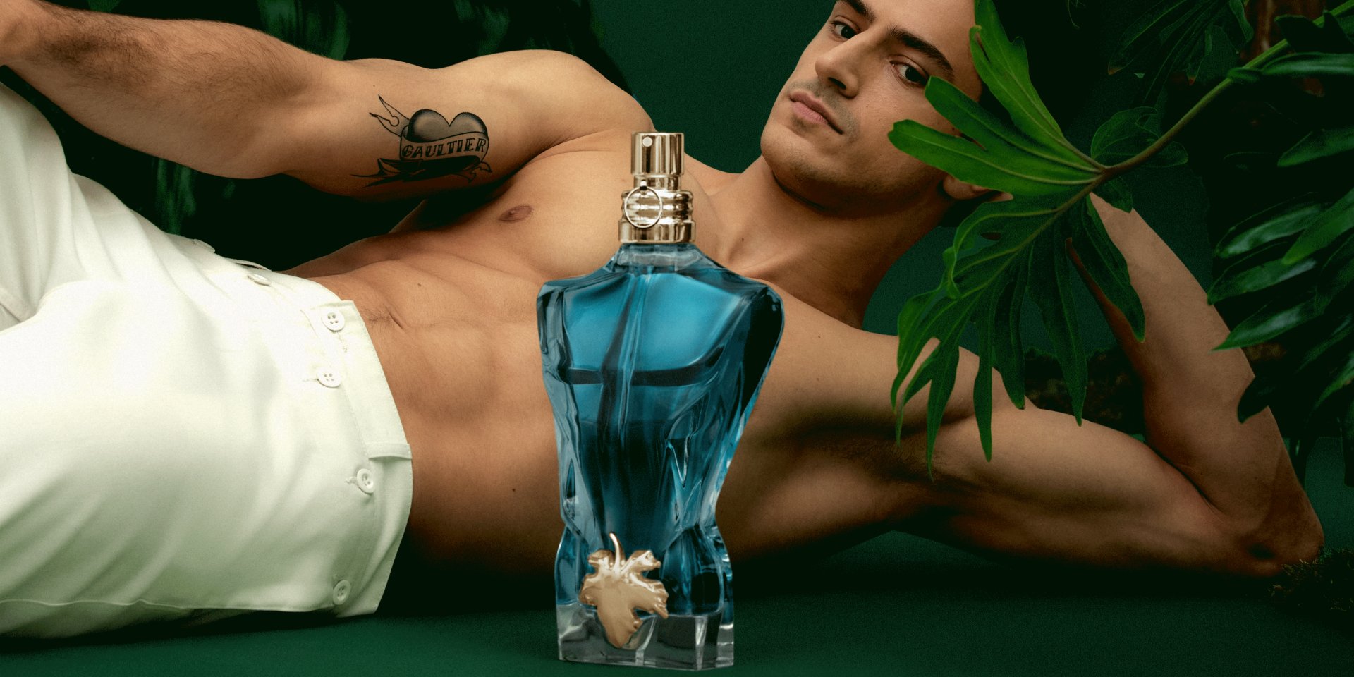 Male model with Le Beau EDT bottle on dark green background